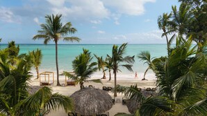 A beach with thatched umbrellas, lounge chairs, and palm trees. - Impressive Premium Punta Cana (Punta Cana)