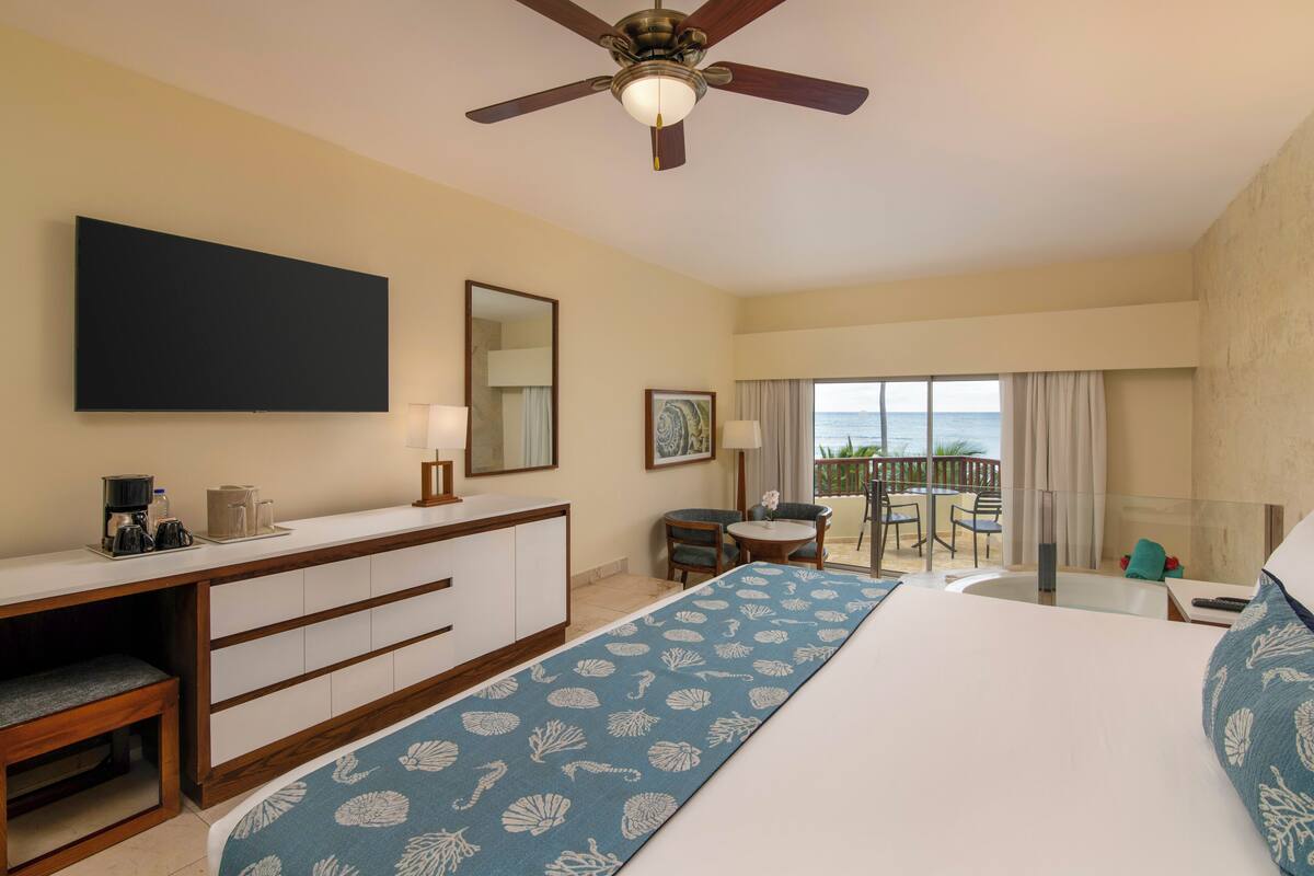 Ein Hotelzimmer mit Bett, Schreibtisch, Stuhl, einem Balkon mit Blick und Deckenventilator.
