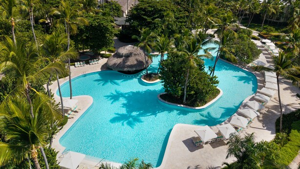 A resort pool with a tropical setting, surrounded by palm trees and a view of the ocean. - Impressive Premium Punta Cana (Punta Cana)