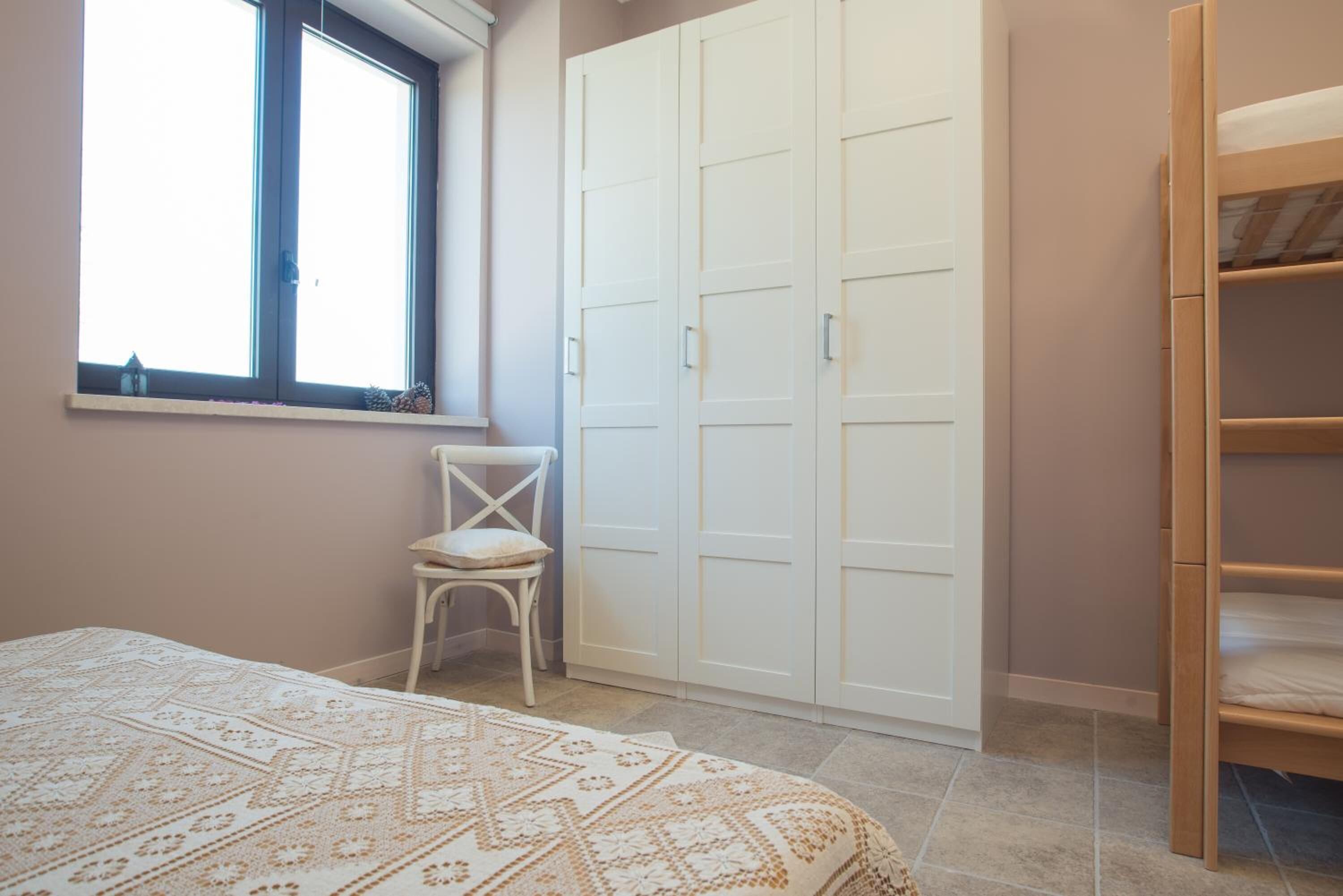 A bedroom with a bed, a chair, a wardrobe, and a window.
