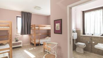 A room with bunk beds, a small table with flowers, a chair, and a bathroom with a toilet and sink.