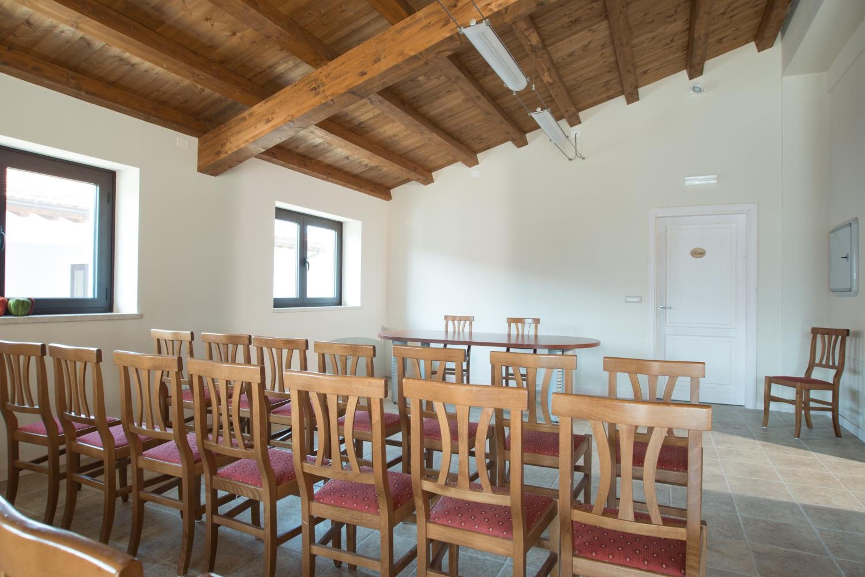 Un comedor con sillas y mesas de madera, un alto techo de madera y ventanas con persianas.