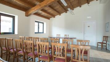 Un comedor con sillas y mesas de madera, un alto techo de madera y ventanas con persianas.