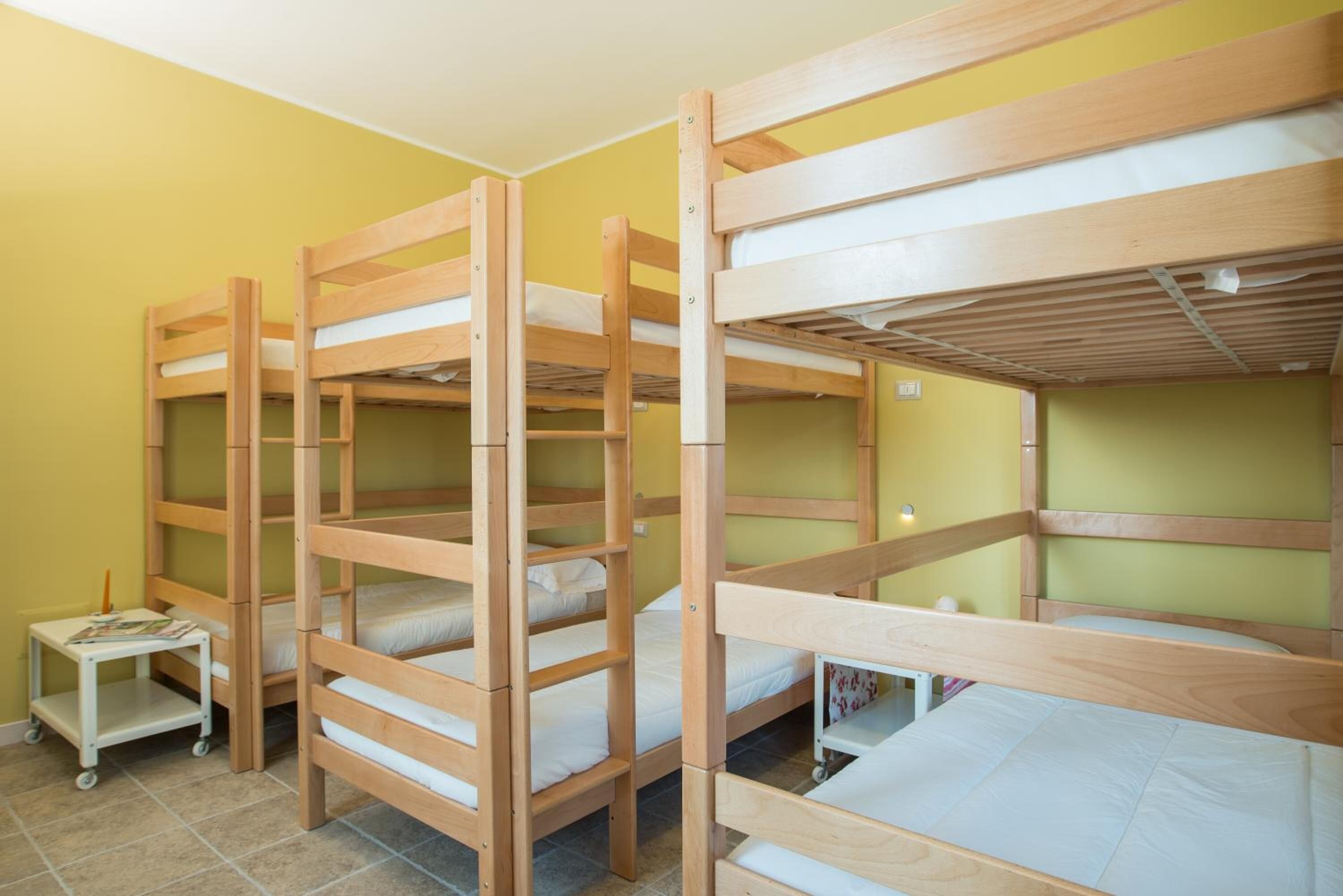 Une chambre de dortoir avec des lits superposés, une petite table avec un magazine et une étagère fixée au mur.