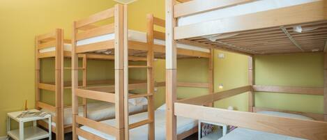 Une chambre de dortoir avec des lits superposés, une petite table avec un magazine et une étagère fixée au mur.