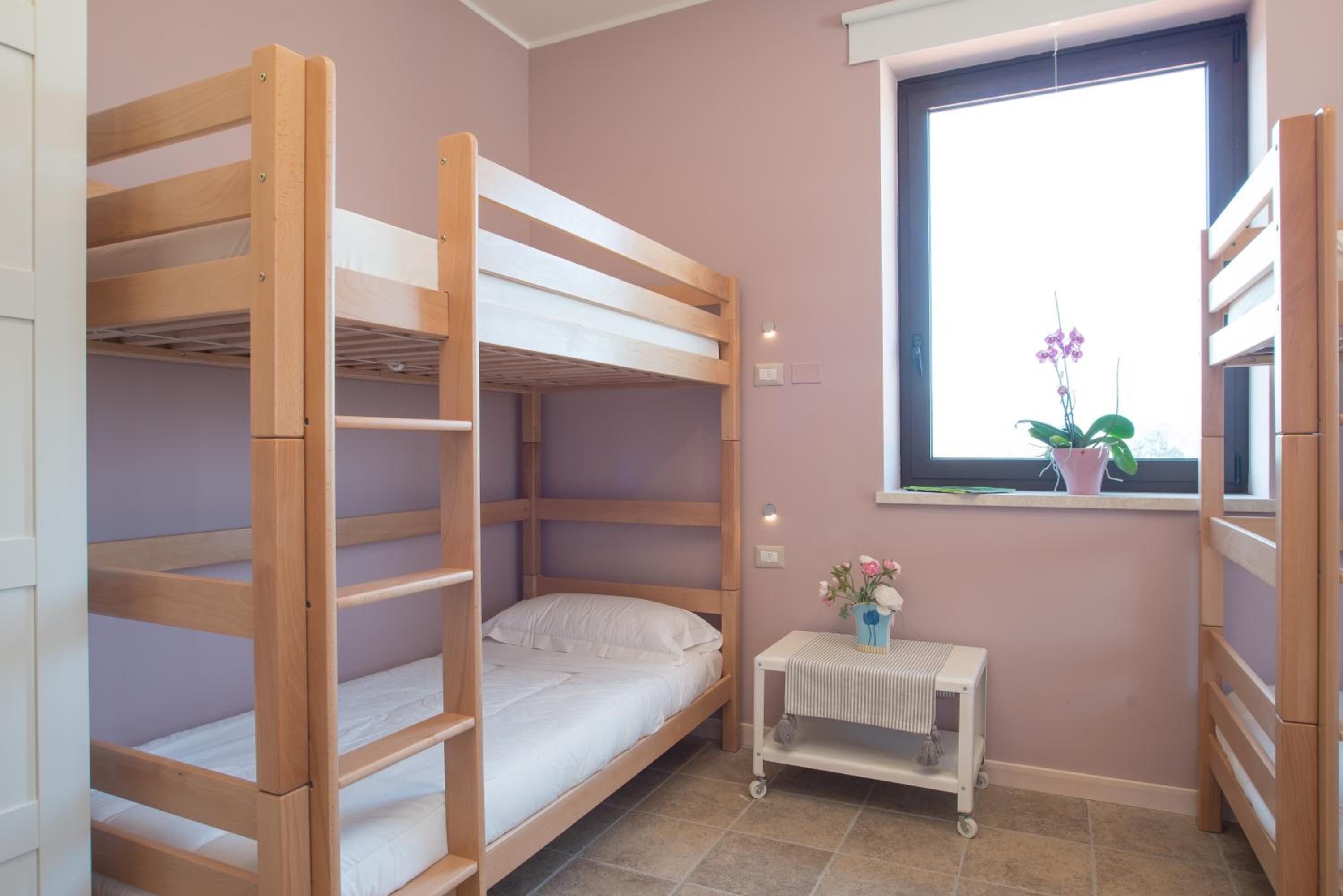Dormitorio con literas, una ventana, una pequeña mesa con una planta y piso de baldosas.