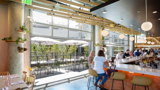 An indoor dining area with a bar, wooden beams, and large windows. - The Source Hotel (Denver)