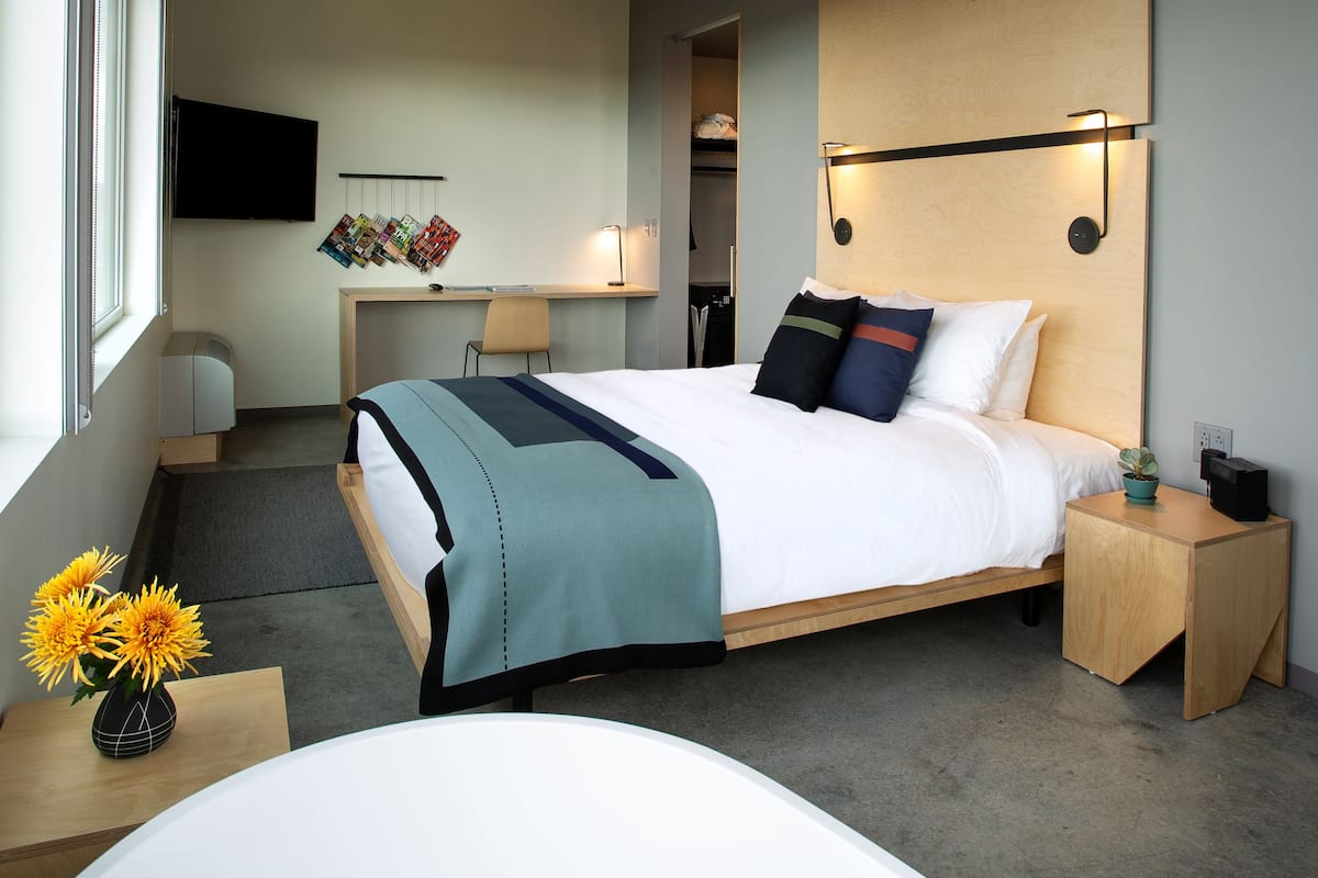 A modern bedroom with a large bed, bedside tables, a desk, and a TV mounted on the wall.