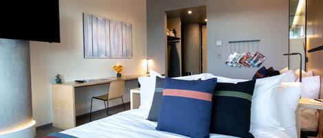 A modern hotel room with a large bed, a desk, and a flat-screen TV.