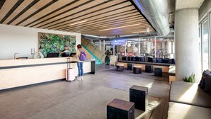 A modern lobby with a wooden ceiling, a reception desk, a staircase, and seating areas. - The Source Hotel (Denver)