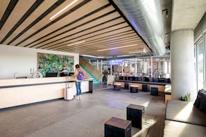 A modern lobby with a wooden ceiling, a reception desk, a staircase, and seating areas. - The Source Hotel (Denver)