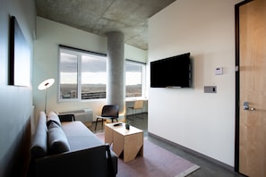A modern living room with a sofa, a coffee table, a TV, and a large window offering a view of the city.