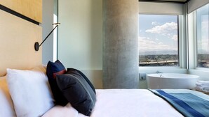 A modern hotel room with a large bed, a round bathtub, and a city view. - The Source Hotel (Denver)