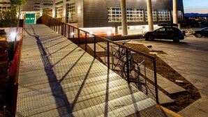 A modern multi-story building with a covered entrance and a ramp leading to the main entrance. - The Source Hotel (Denver)