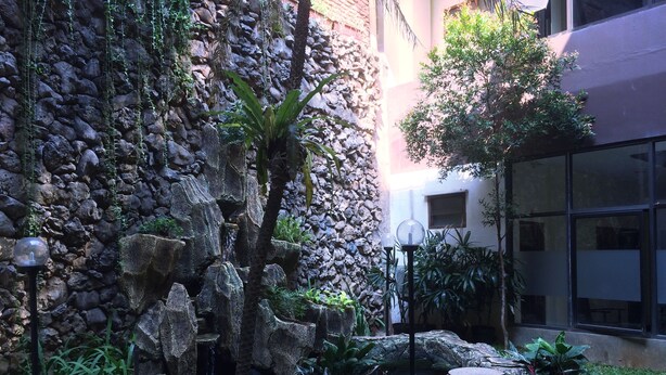 Un jardín con muro de piedra, una cascada pequeña y un sendero con piedras.