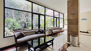 A spacious indoor area with large windows, a sofa, a chair, and a trash bin. - Hotel Nusantara Indah Syariah (Jakarta)