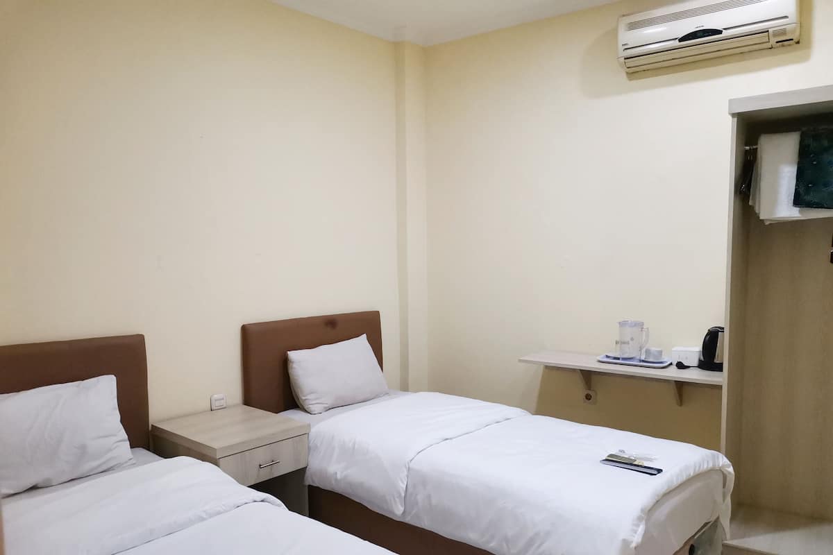 Habitación de hotel con dos camas individuales, un escritorio pequeño con cafetera y un televisor montado en la pared.