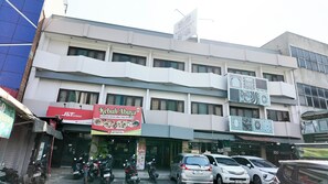 A multi-story building with commercial signage, a parking area, and a row of parked cars. - Hotel Nusantara Indah Syariah (Jakarta)