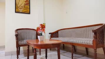 A living room with a wooden sofa, two armchairs, a small round table, and a potted plant.