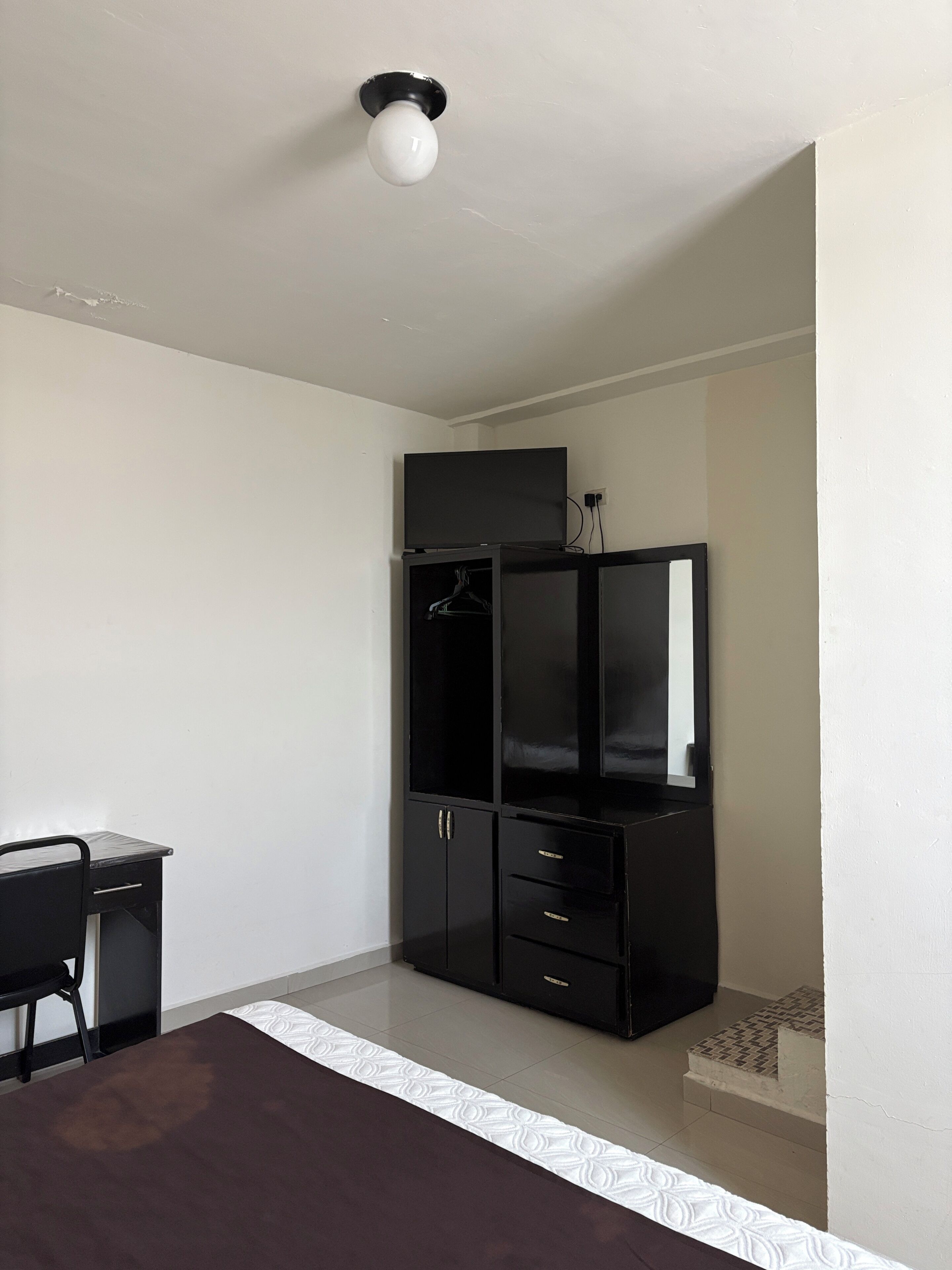 A room with a black wardrobe, a desk, and a white patterned rug.