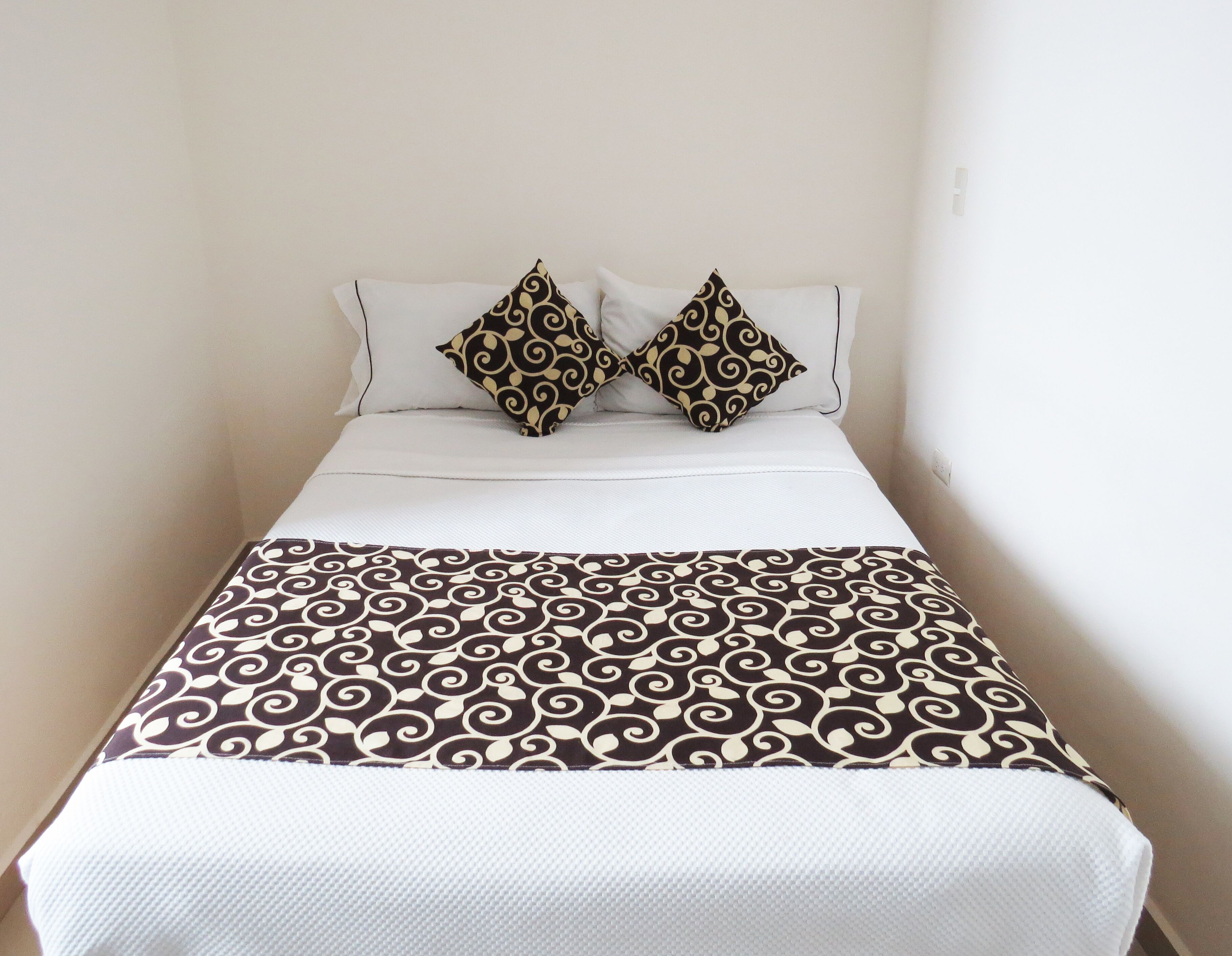Una cama bien hecha con un edredón estampado y dos almohadones decorativos.