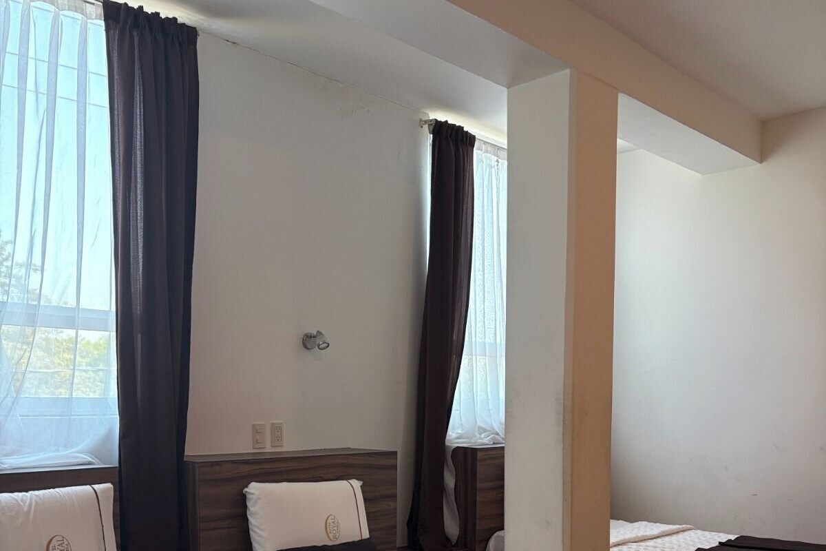 A hotel room with three beds, each with a dark headboard and white bedding.