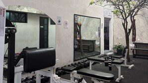 Een sportschool met trainingsapparatuur, spiegels en een boom.
