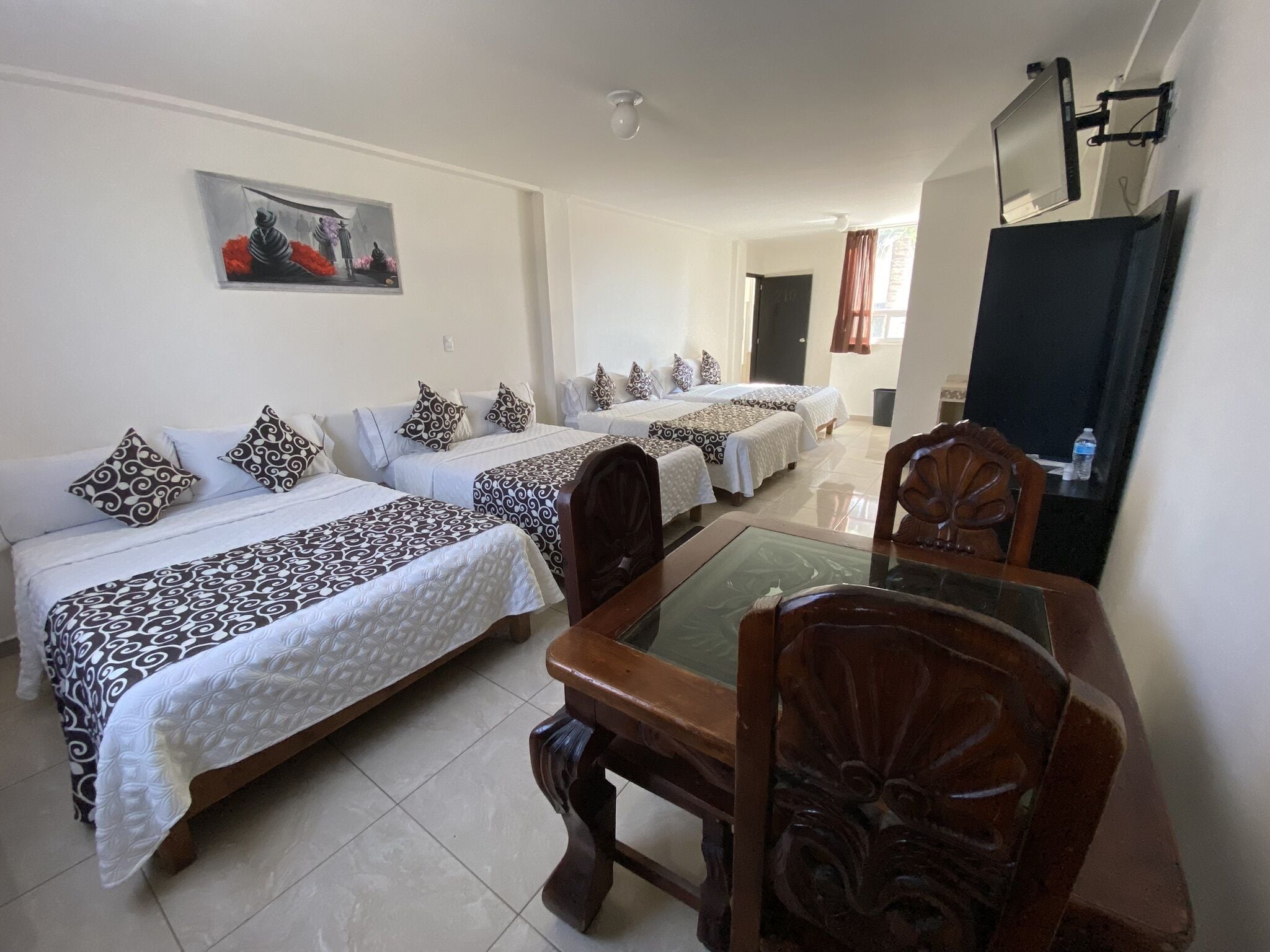 A hotel room with two single beds, a dining table with chairs, a painting on the wall, and a TV mounted on the wall.