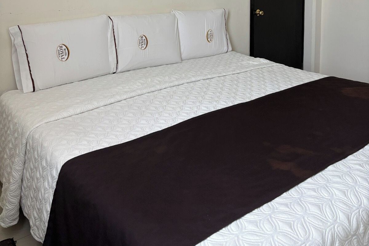 A bed with a white and dark-colored bedspread, a white headboard with pillows, and a black door.