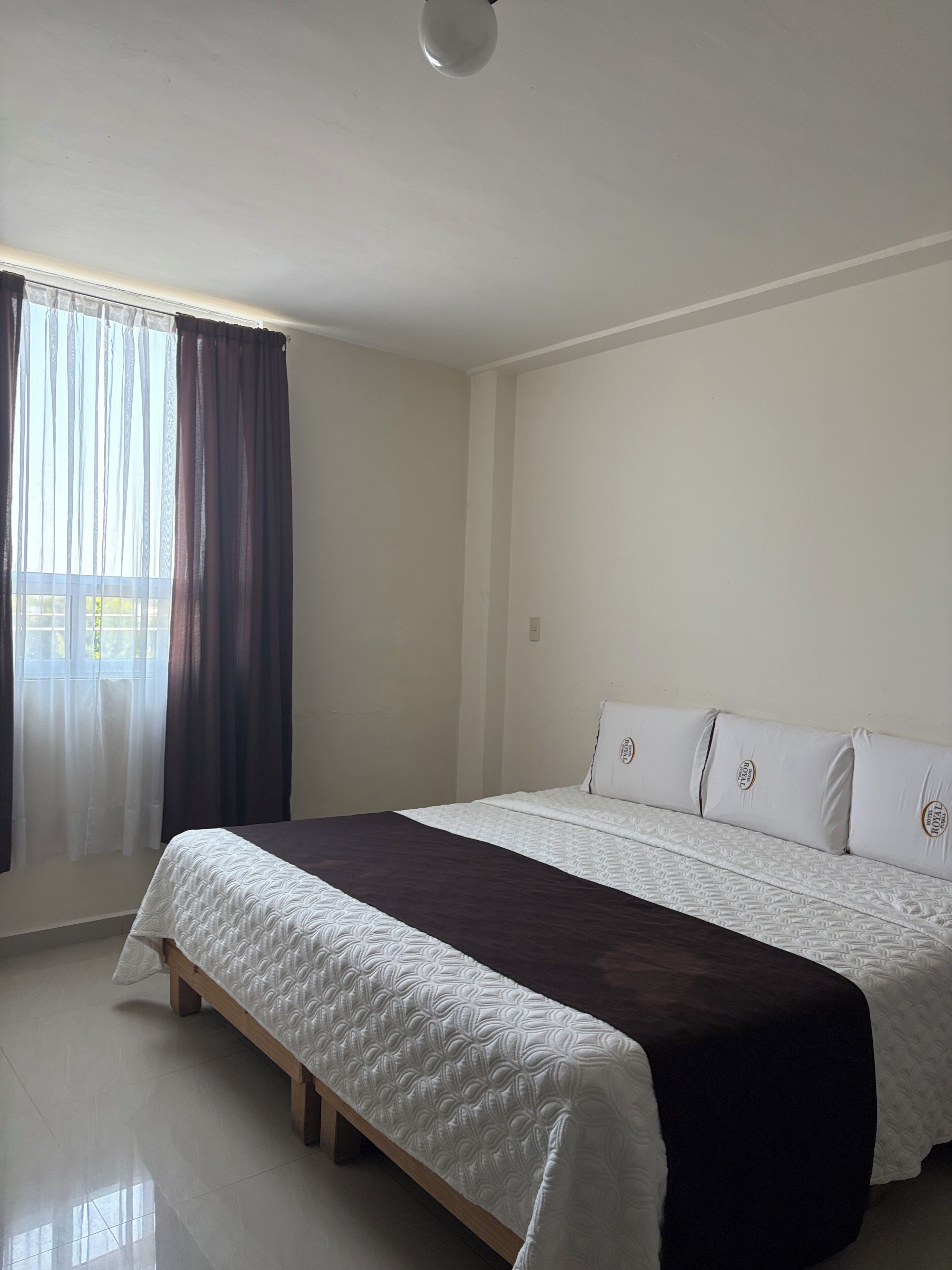 Un dormitorio con cama, una ventana con cortinas y una lámpara.