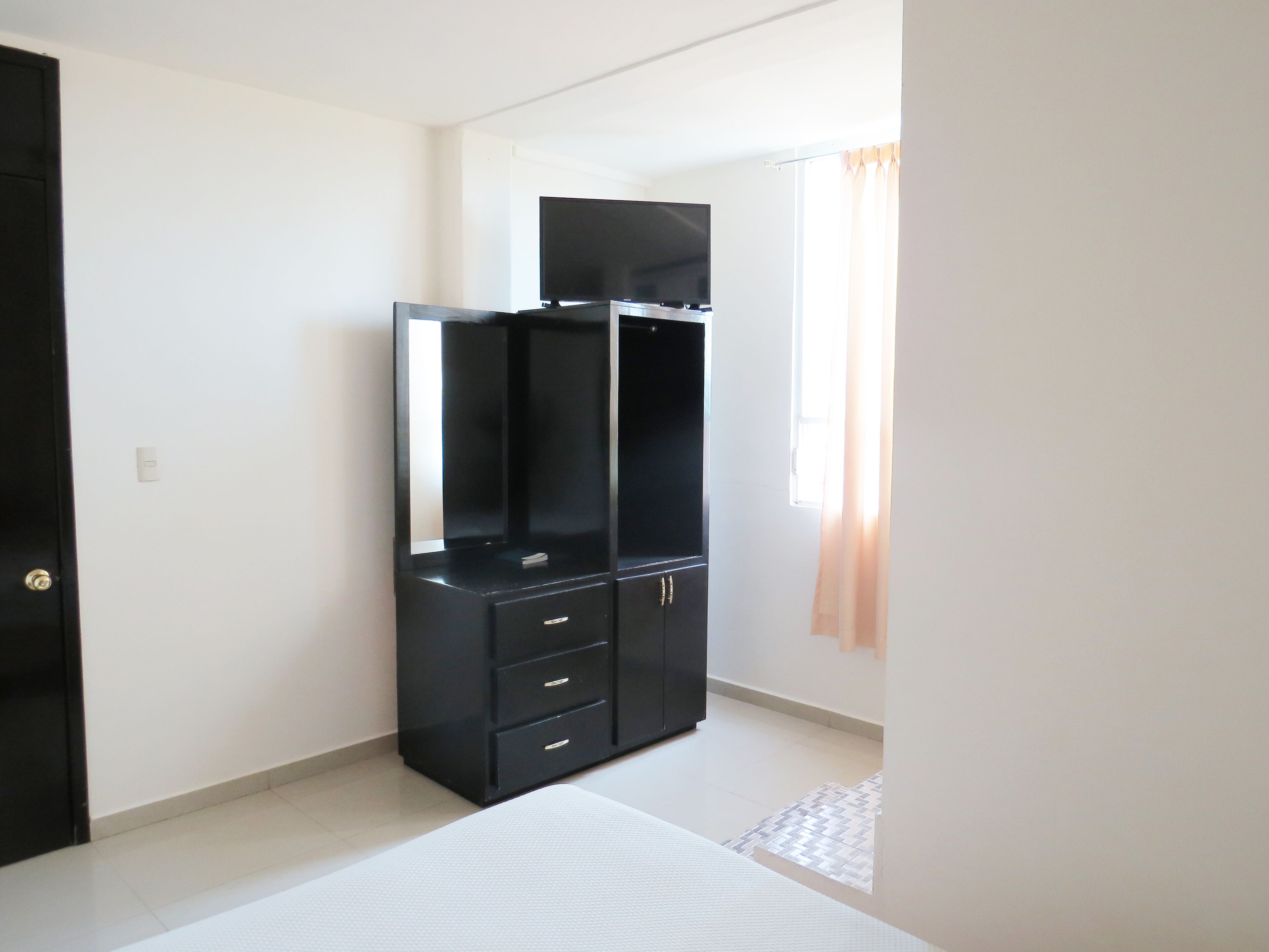 Une pièce avec une armoire noire, un téléviseur à écran plat, une porte et une fenêtre avec des rideaux.