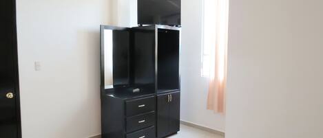 Une pièce avec une armoire noire, un téléviseur à écran plat, une porte et une fenêtre avec des rideaux.
