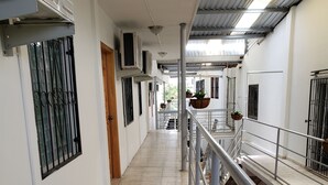 Um corredor com piso de azulejos, corrimãos de metal e unidades de ar condicionado fixadas nas paredes.