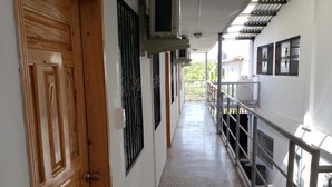 Um corredor com porta de madeira, grades de metal e chão de azulejos.
