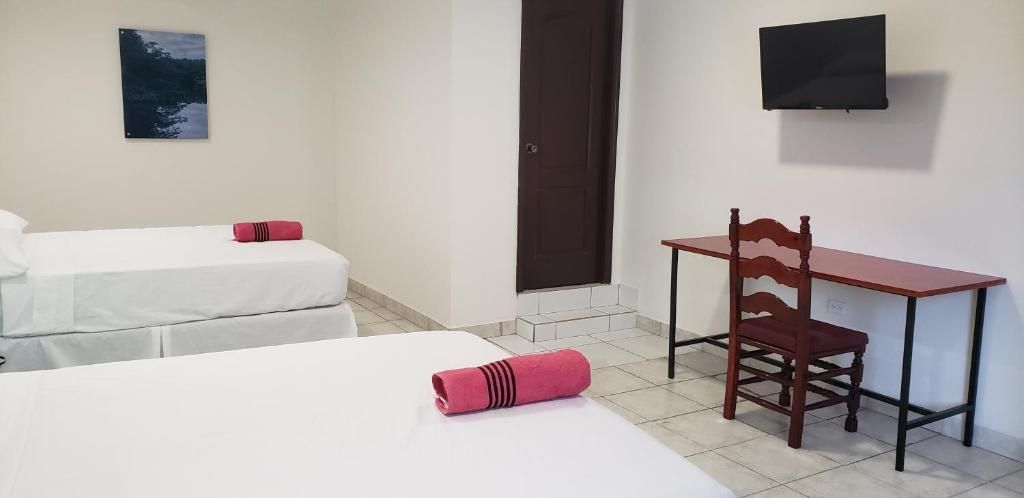 Habitación de hotel con dos camas, un escritorio, una silla, un televisor y una puerta.