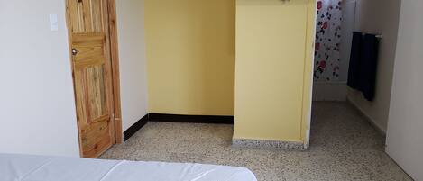 Una habitación con una cama, una puerta de madera, un televisor y una zona de ducha.