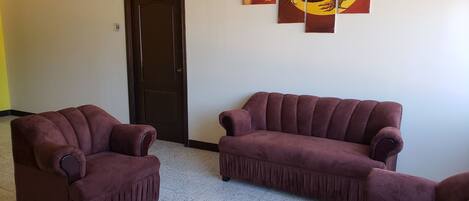 Una habitación con dos sillones y un sofá, una puerta, y tres obras de arte colgadas en la pared.