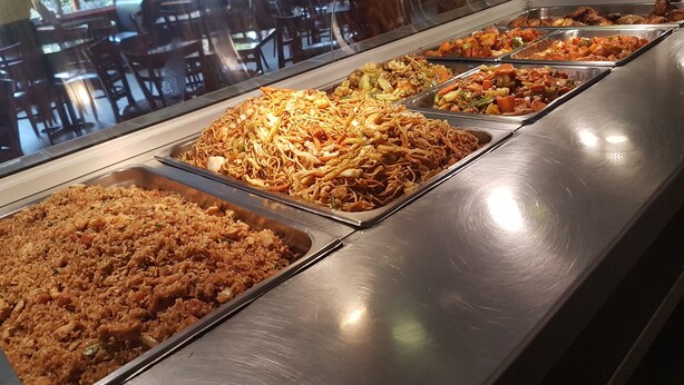 Buffet com diversos pratos, incluindo arroz frito, macarrão e legumes variados.