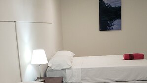 Quarto de hotel com duas camas, uma mesa de cabeceira, uma luminária e um quadro na parede.