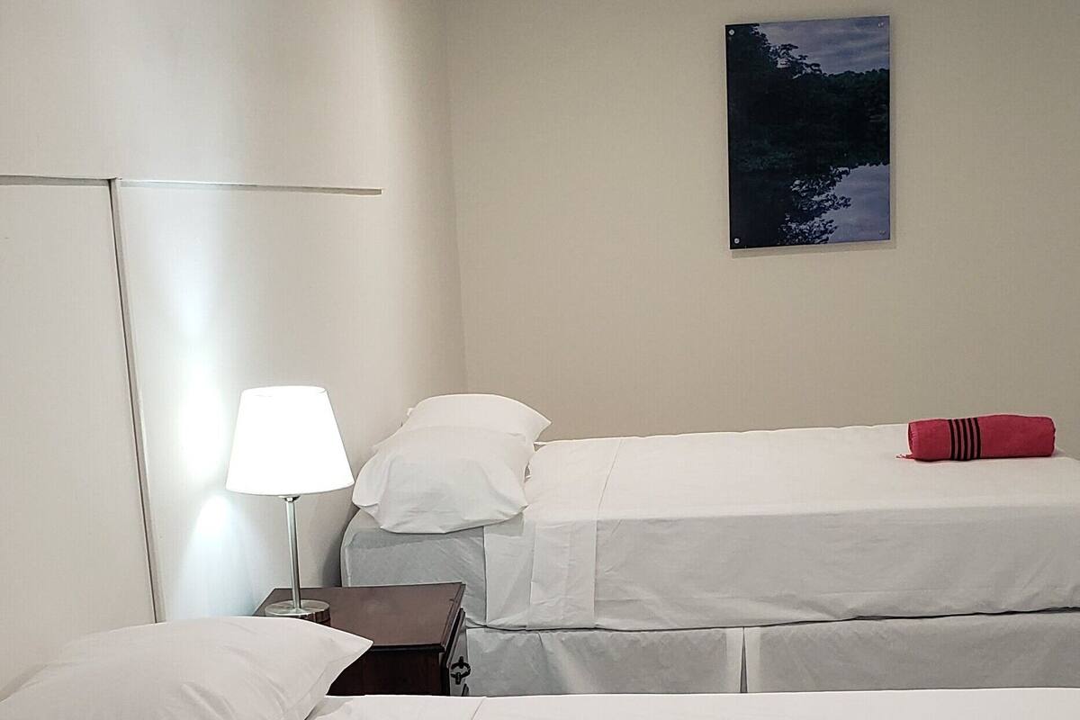 Een hotelkamer met twee bedden, een nachtkastje, een lamp en een schilderij aan de muur.