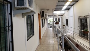 Corredor com aparelhos de ar condicionado, grades de metal e plantas em vasos.