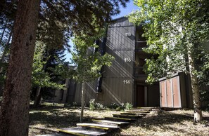 A building with numbered doors, a wooden exterior, and a surrounding area with trees and steps.
