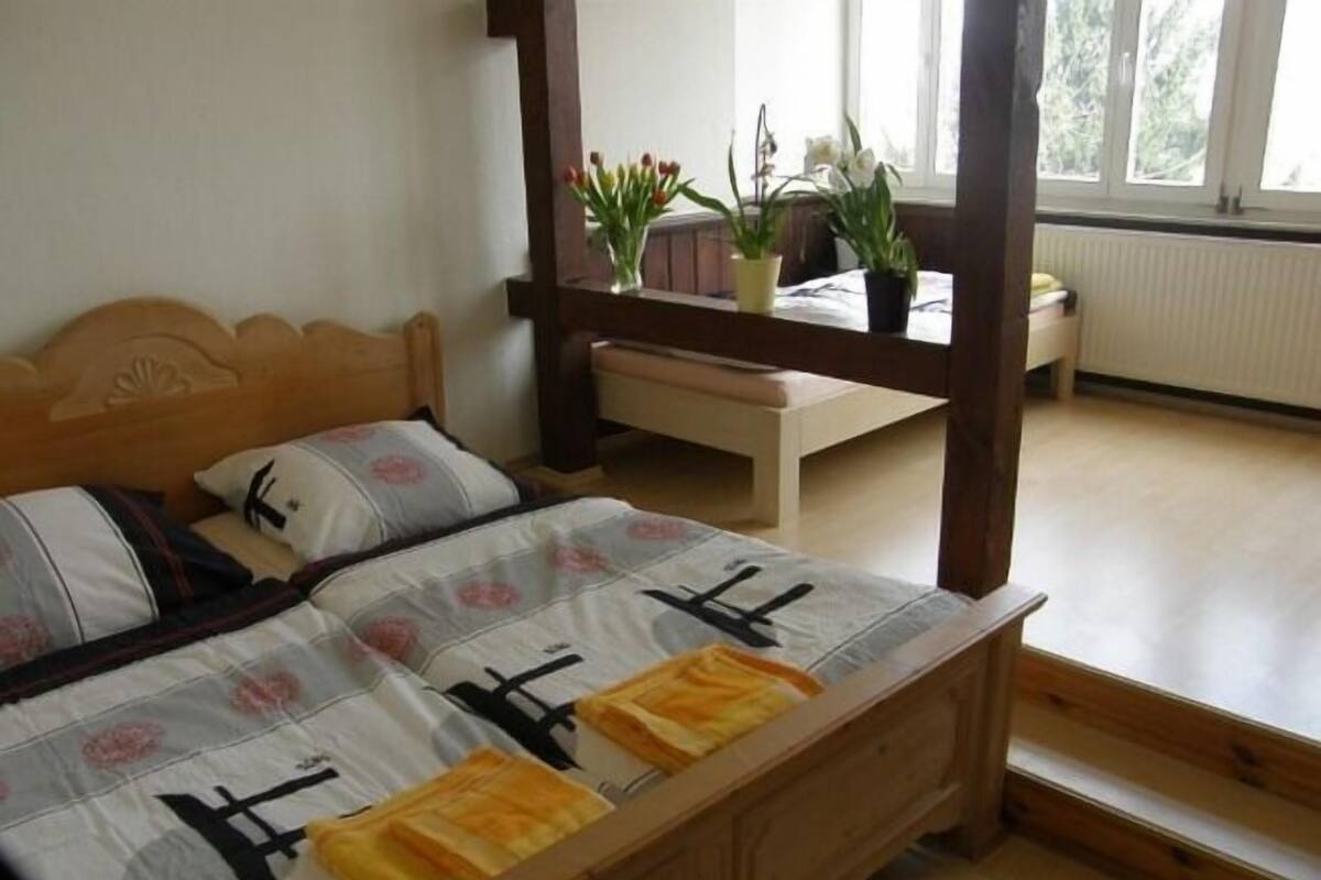 Quarto com cama de madeira, um banquinho e plantas em vasos.