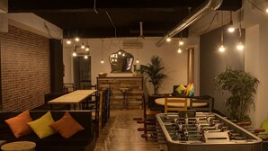 Un espace intérieur accueillant avec un baby-foot, un coin salon doté de coussins et des luminaires suspendus.