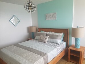 A neatly made bed with patterned bedding, two bedside lamps, a decorative wall piece, and a hanging light fixture.