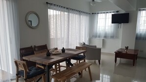 A spacious living area with a wooden dining table, comfortable seating, a ceiling fan, and a flat-screen TV mounted on the wall. - KSL Residence (Boca Chica)