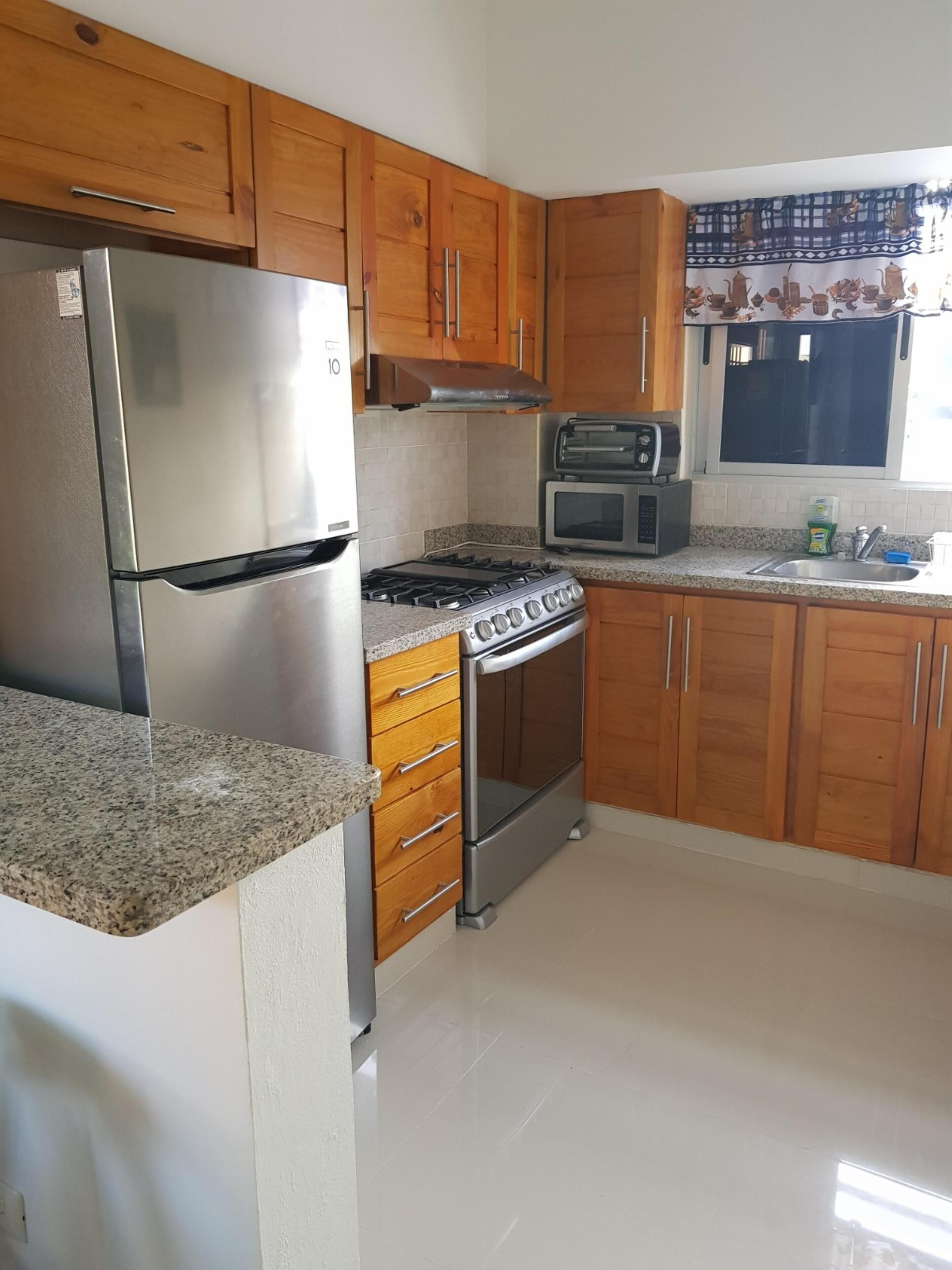 Cozinha com armários de madeira, geladeira de aço inoxidável, fogão a gás, micro-ondas e torradeira.