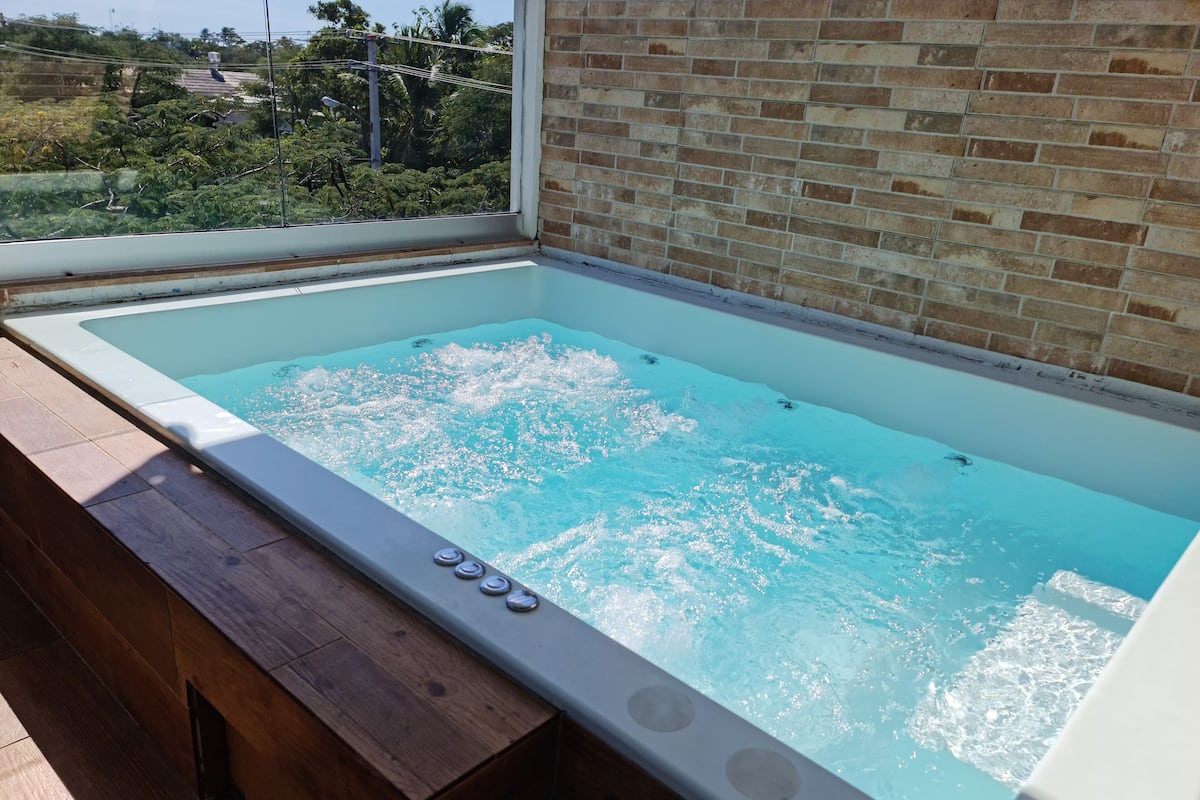 A hot tub with a view of a brick wall and greenery outside.