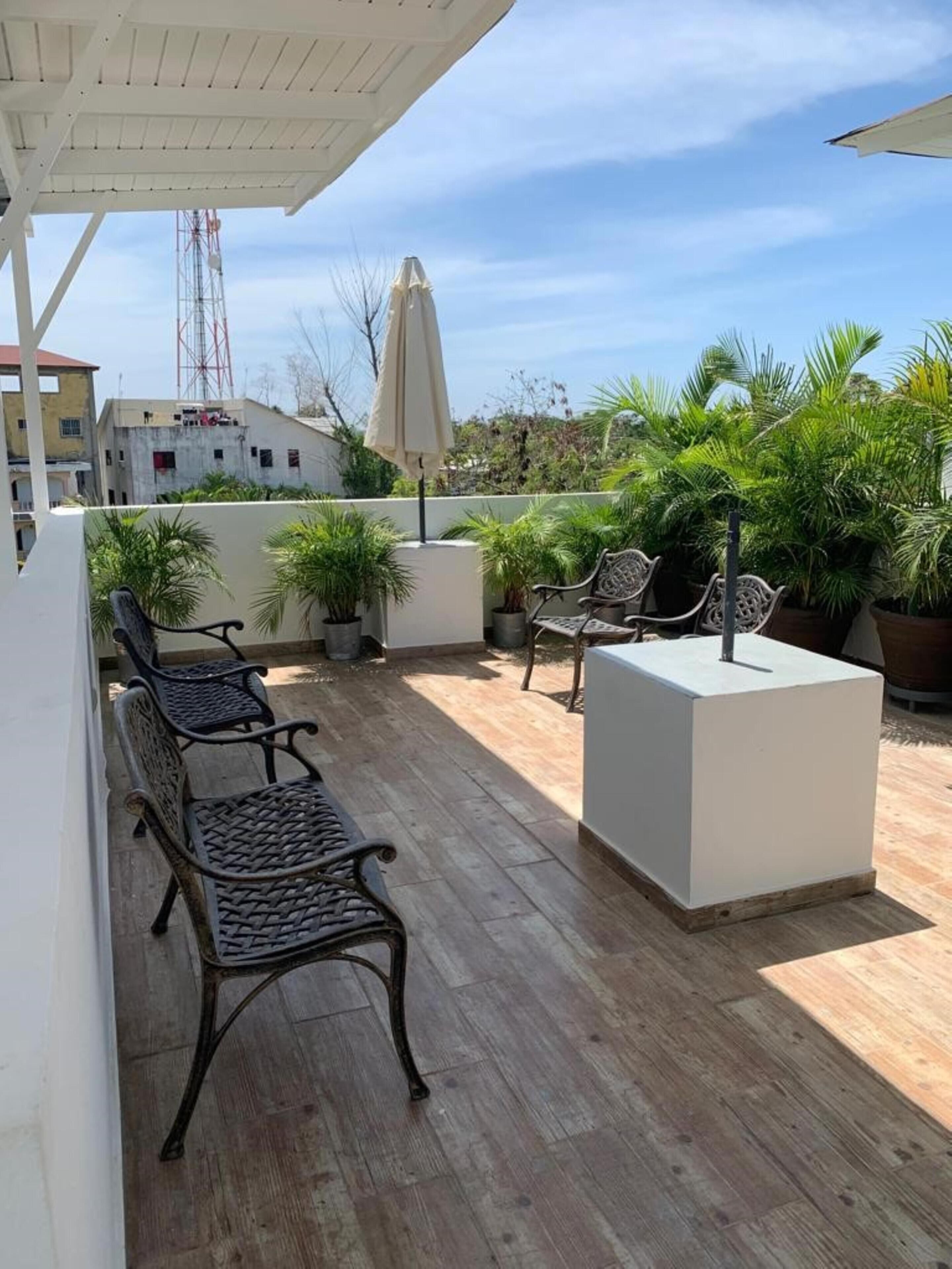 A rooftop patio with wooden flooring, two black metal chairs, a white planter, and an umbrella.