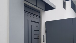 A modern building entrance with a grey door and a small step leading to a doormat. - KSL Residence (Boca Chica)